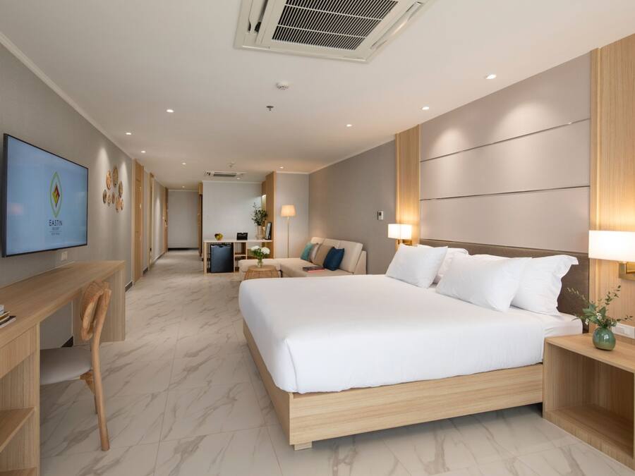 A modern hotel room with a large bed, a desk, and a television on the wall.