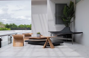 Un espace extérieur moderne, aménagé avec des tabourets en bois et un fauteuil noir, agrémenté d’une plante en pot et offrant une vue sur la verdure.