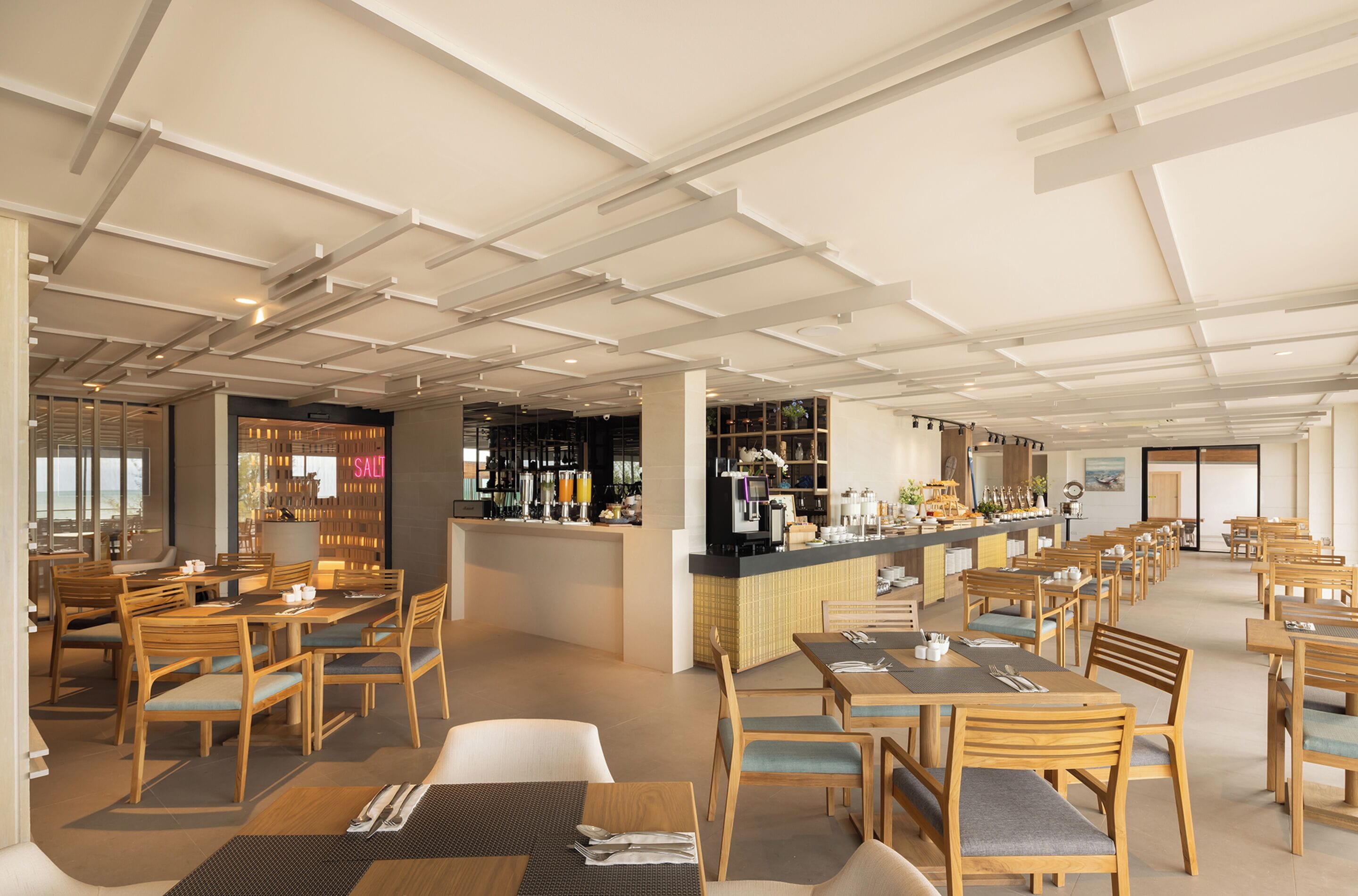 Un restaurante espacioso con mesas y sillas de madera, una zona de bar y vistas a la ciudad.