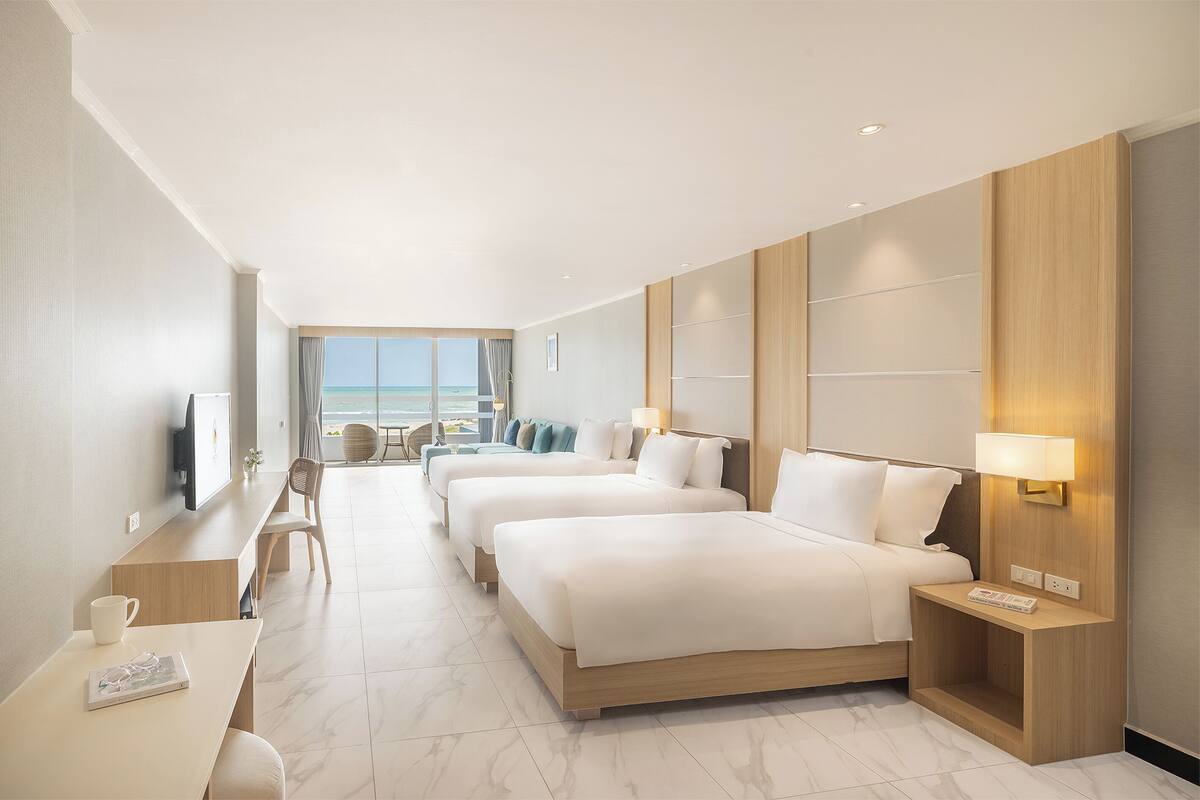 A hotel room with three beds, a desk, a chair, and a TV.