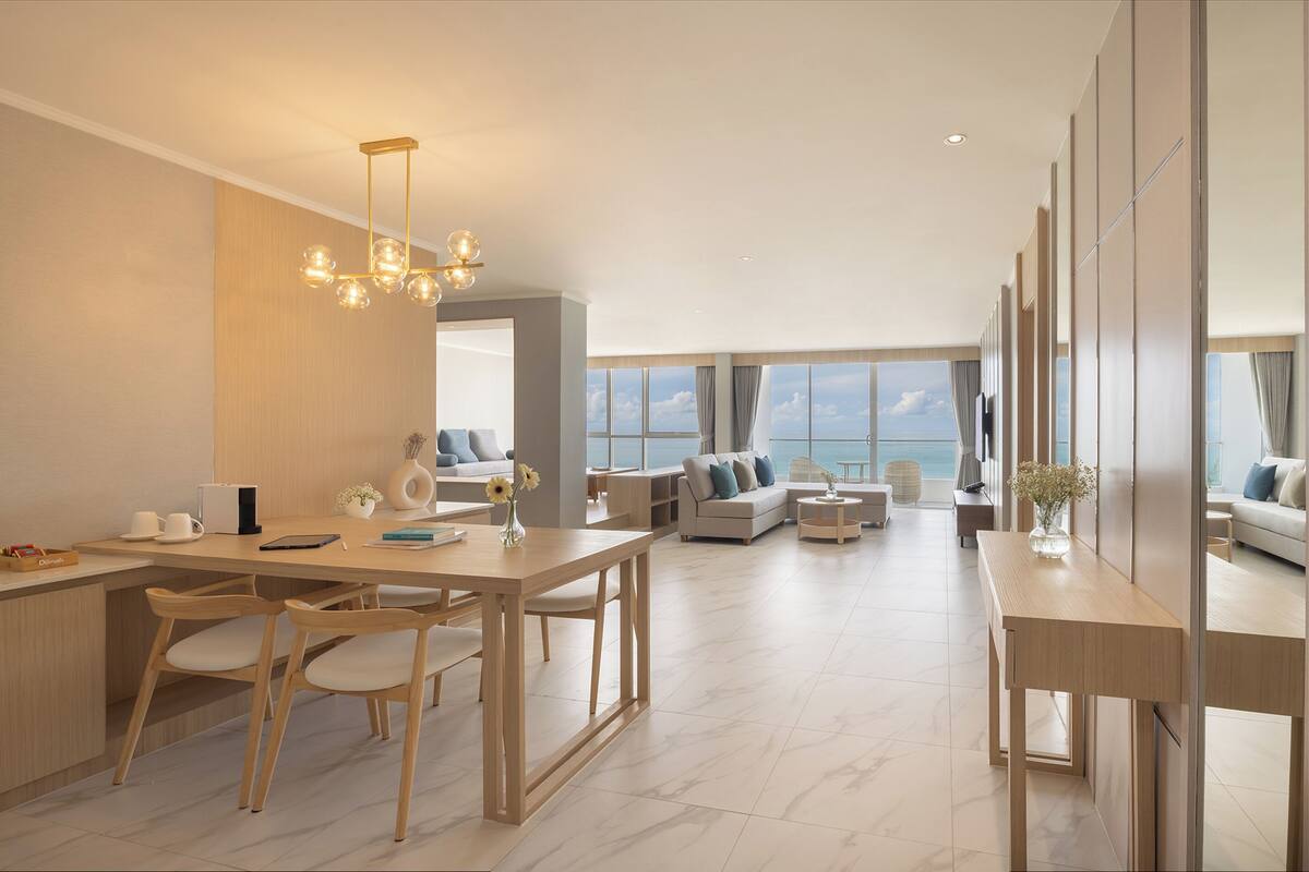 A modern living room with a dining area, large windows, and a view of the sea.