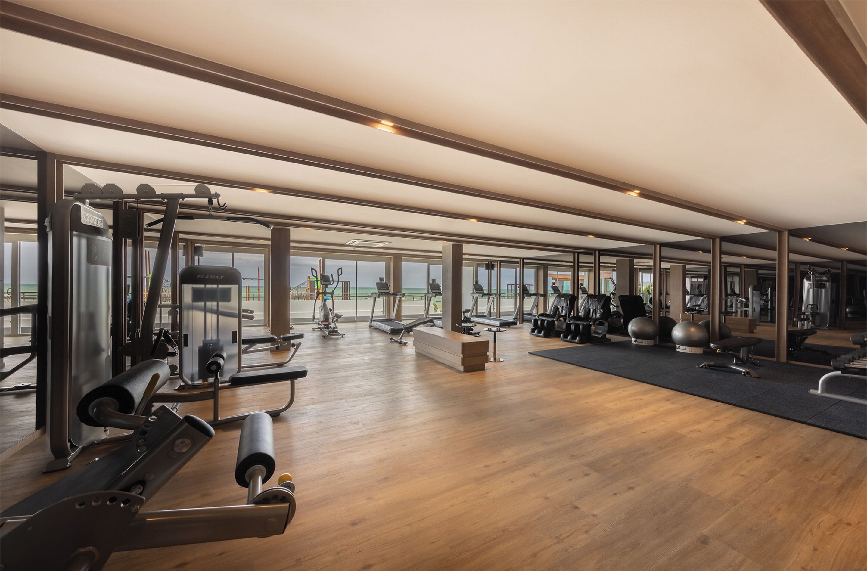 Une salle de sport spacieuse, dotée de divers appareils d’exercice, de grandes fenêtres offrant une vue sur l’extérieur et d’un plancher en bois.