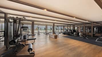 Une salle de sport spacieuse, dotée de divers appareils d’exercice, de grandes fenêtres offrant une vue sur l’extérieur et d’un plancher en bois.