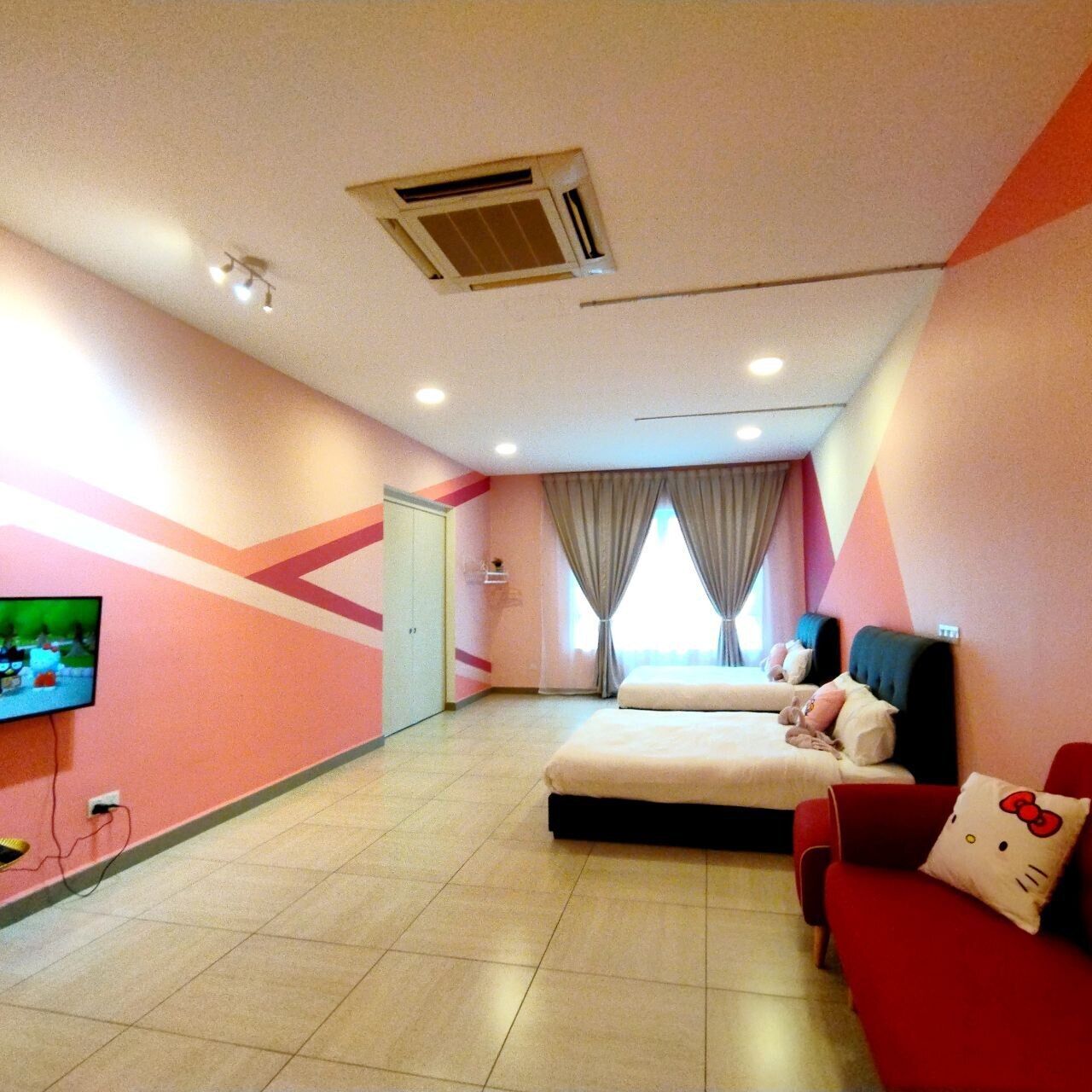 A hotel room with a bed, a TV, a red chair, and a window with curtains.