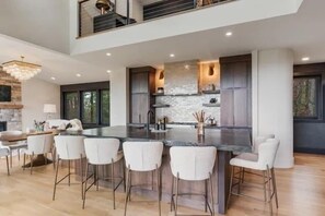 A modern kitchen with a central island, bar stools, and a dining area with a chandelier.