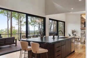 A modern kitchen with a large island, bar stools, and a view of the outdoors. - Brevard's Cedar Mountain Retreat | 4BR Mountain Views | Hot Tub + Sauna | Near DuPont (Brevard)