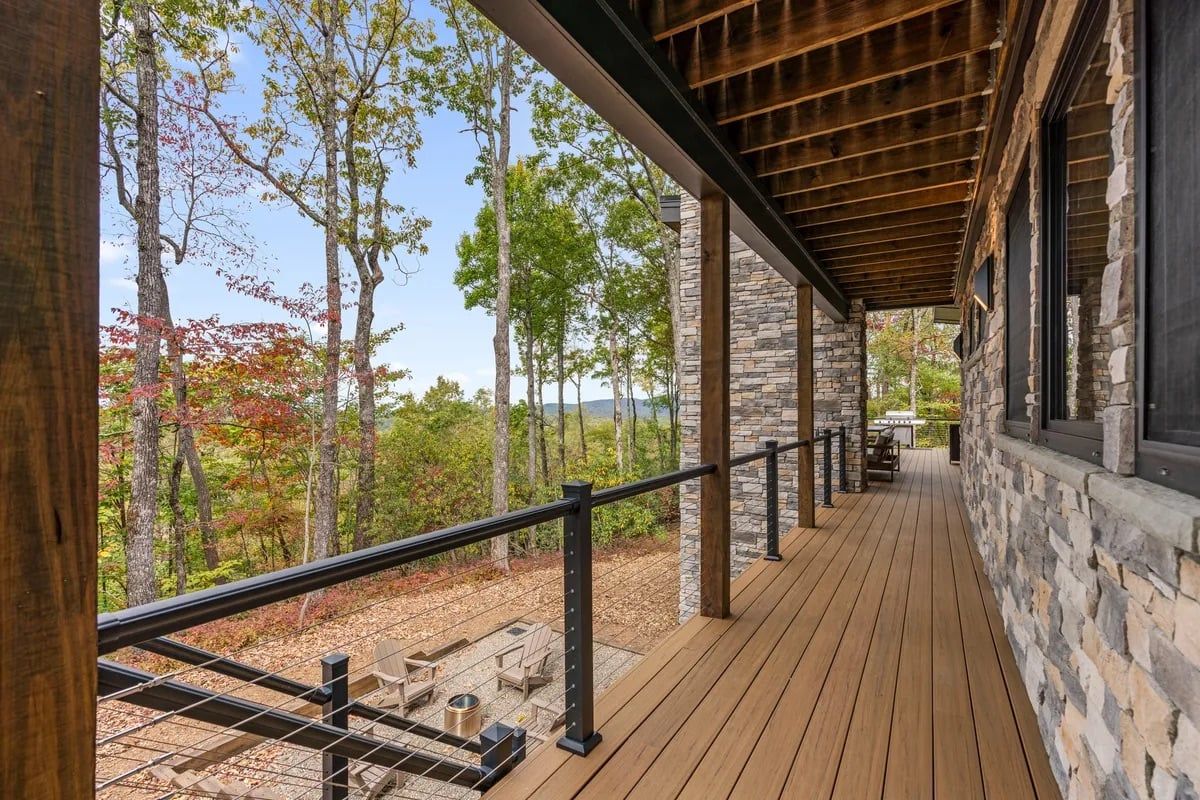 A wooden deck with a stone wall, a railing, and a view of trees.