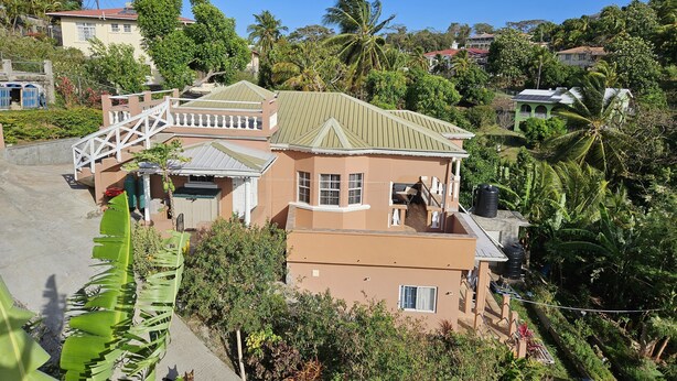 Et tosyltet hus med balkon, omgivet af frodig vegetation og palmer.