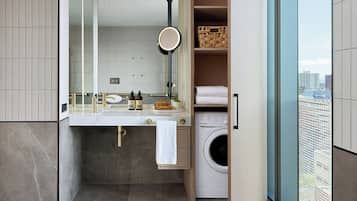 A modern bathroom with a built-in washer and dryer, a large mirror, and a view of the city through a glass door.