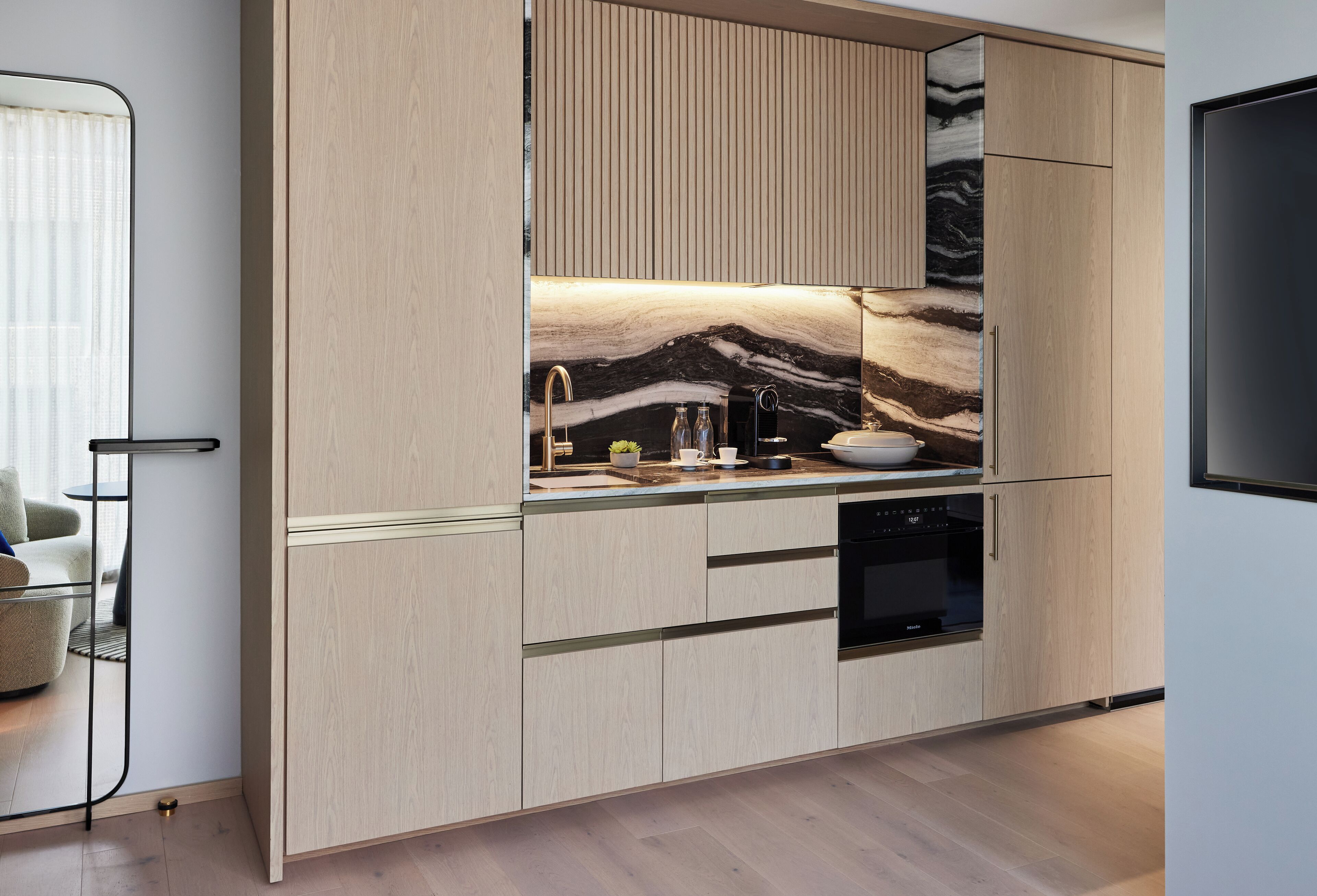 Une cuisine moderne avec des meubles en bois clair, un pare-feu en marbre et des appareils électroménagers intégrés.