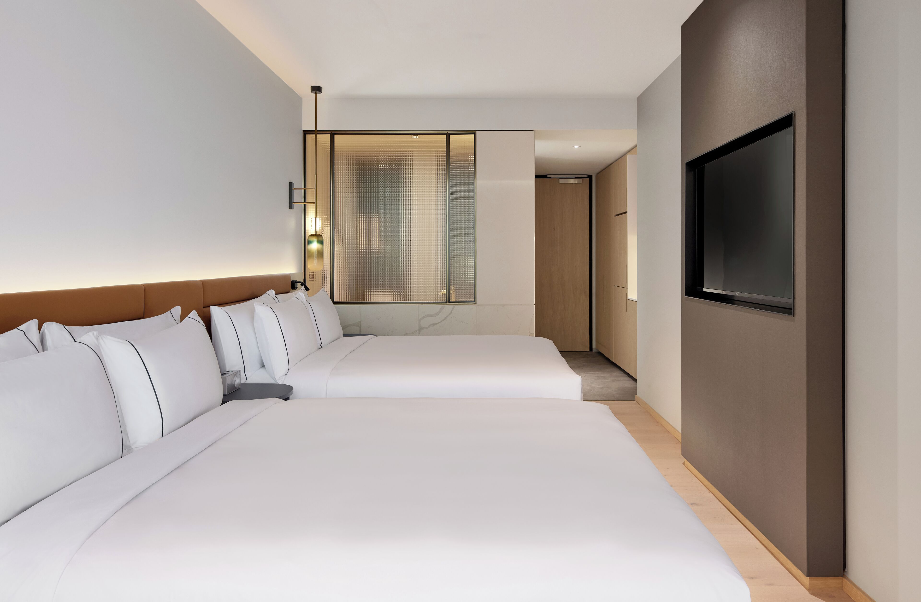 A hotel room with two beds, a TV on the wall, and a large window with curtains.