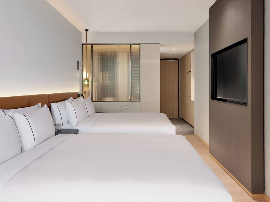 Habitación de hotel con dos camas, un televisor en la pared y un ventanal con cortinas.