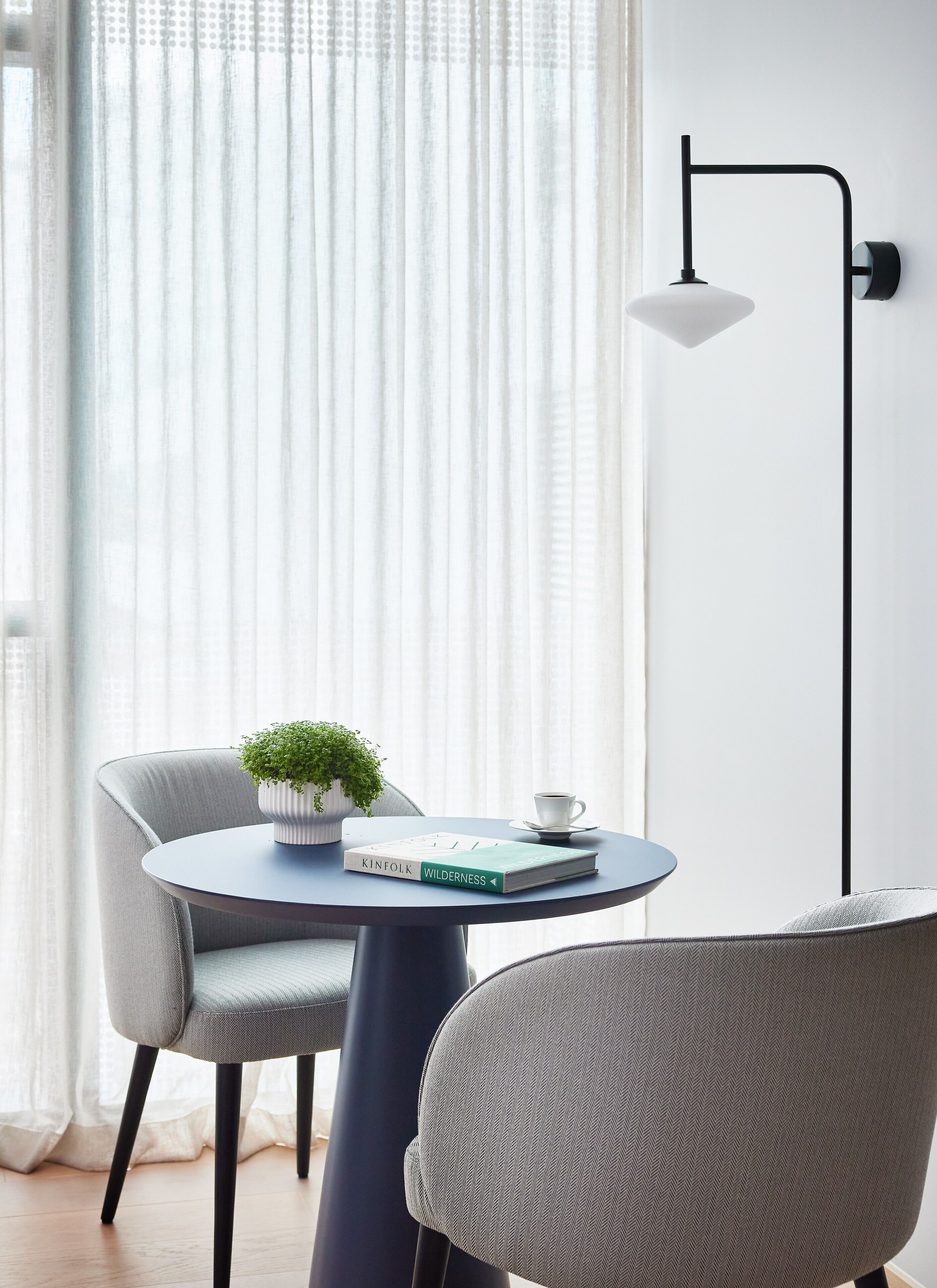 A modern room with a round table, two chairs, a potted plant, a book, a cup, and a floor lamp.