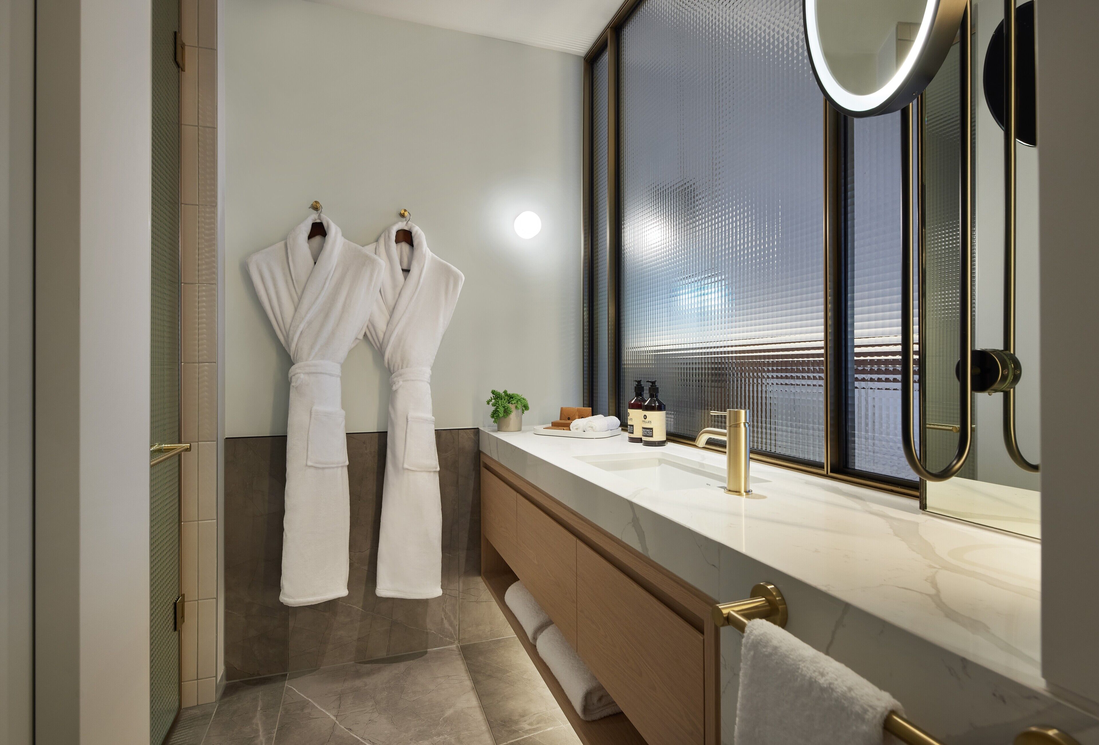 A modern bathroom with a large mirror, a bathtub, and two white robes hanging on hooks.