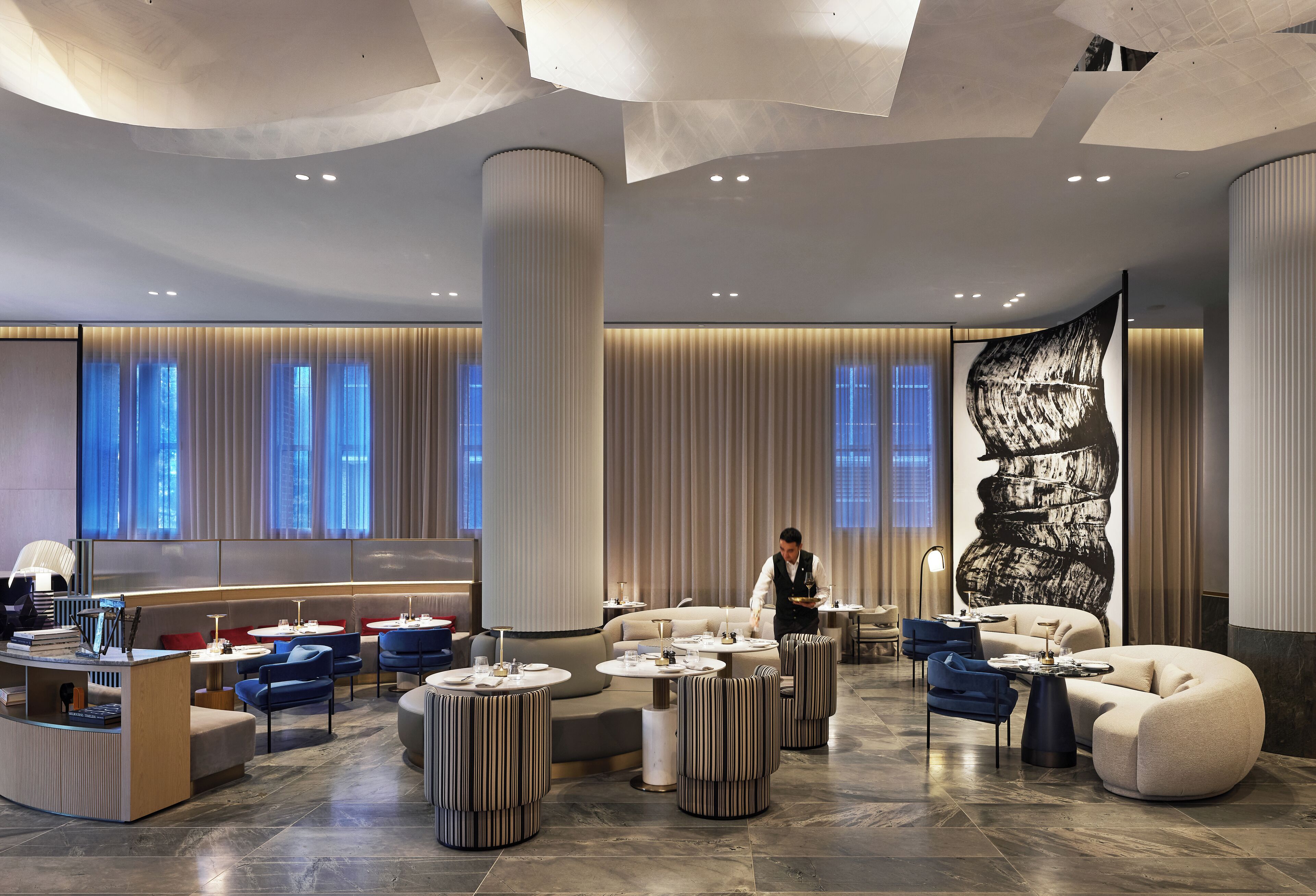 A modern hotel lobby with a reception desk, seating areas, and a large abstract mural.