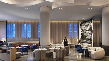 A modern hotel lobby with a reception desk, seating areas, and a large abstract mural.