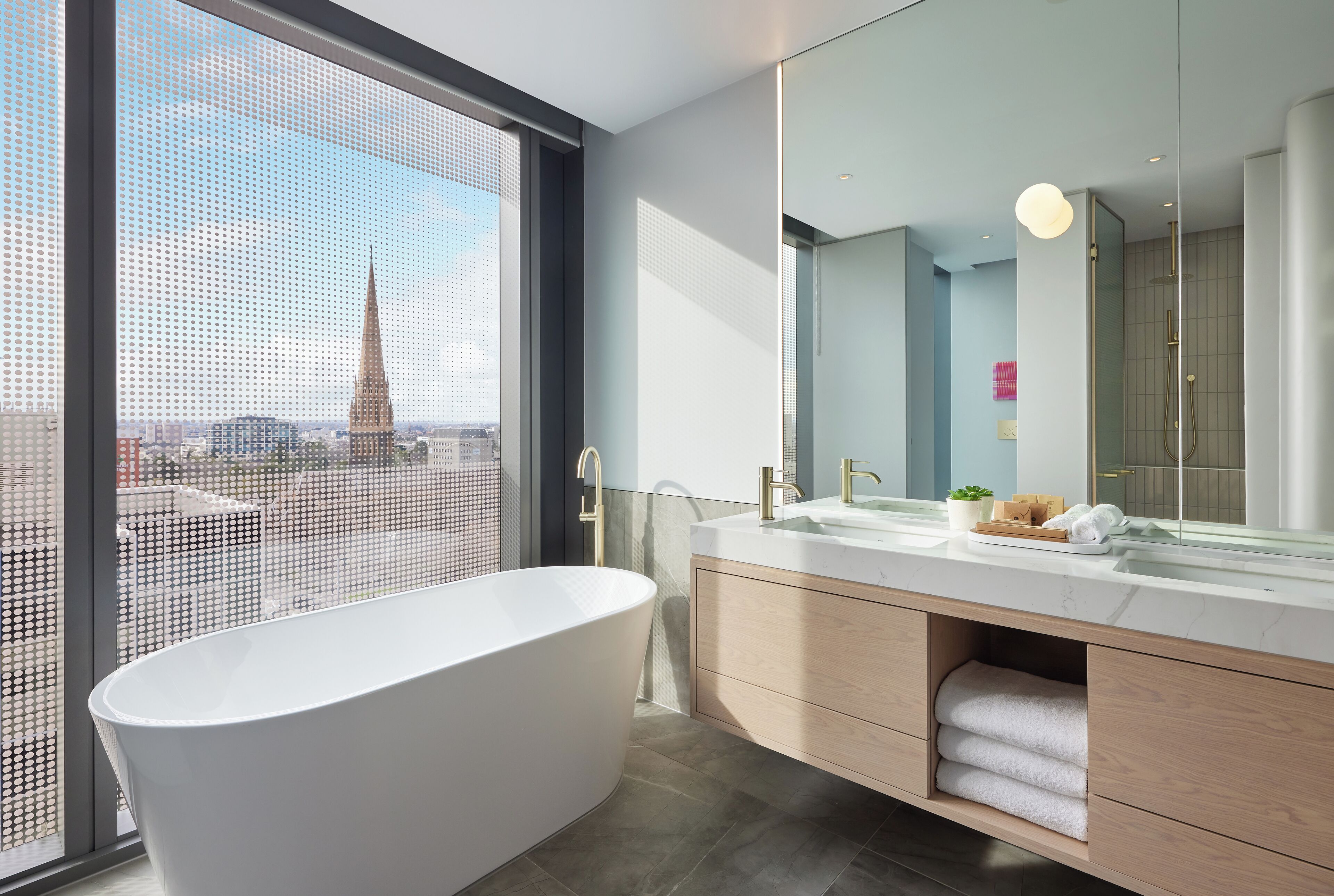 A modern bathroom with a freestanding bathtub, a large mirror, and a view of a cityscape through a large window.