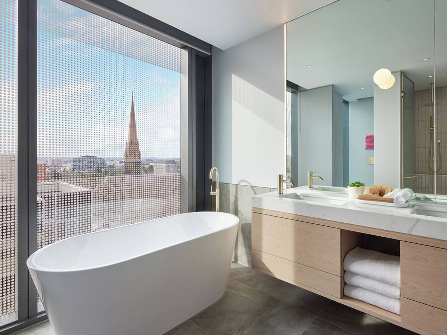 A modern bathroom with a freestanding bathtub, a large mirror, and a view of a cityscape through a large window.
