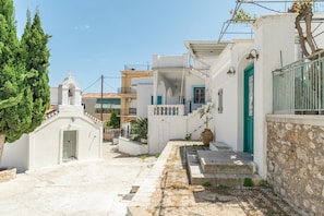 A narrow street with white buildings, a church, and a tree.