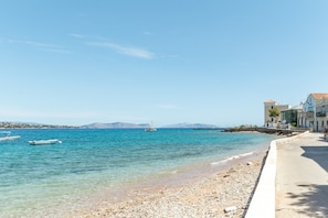 A beach with clear water, a boat, and buildings along the shore.