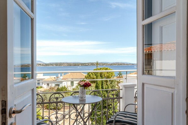 An open balcony with a view of the sea, a table with a vase, and a chair.
