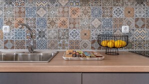 Una cocina con salpicadero de azulejos, un lavamanos de acero inoxidable y una cesta de frutas con limones.
