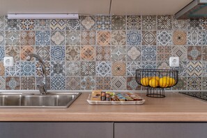 A kitchen with a tiled backsplash, a stainless steel sink, and a fruit basket with lemons.