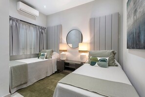 A hotel room with two beds, a round mirror, bedside lamps, a small table, and an air conditioning unit.