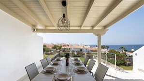 Un área de comedor al aire libre cubierta, con una mesa dispuesta para seis personas, con vista al mar.