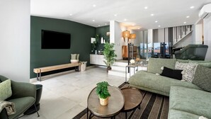 Una sala de estar moderna con un sofá verde, un banco, una mesa de centro con una planta y una escalera que conduce a un nivel superior.