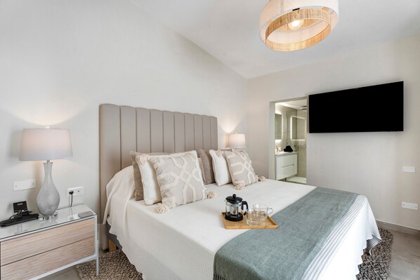 Una habitación de hotel moderna con una cama, mesitas de noche, un televisor de pantalla plana y una cafetera sobre una bandeja.