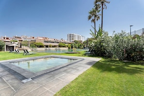 Una piscina amb gandules, una zona enjardinada i un edifici al fons.