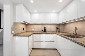 Una cocina moderna con armarios blancos, encimeras de granito y electrodomésticos de acero inoxidable.