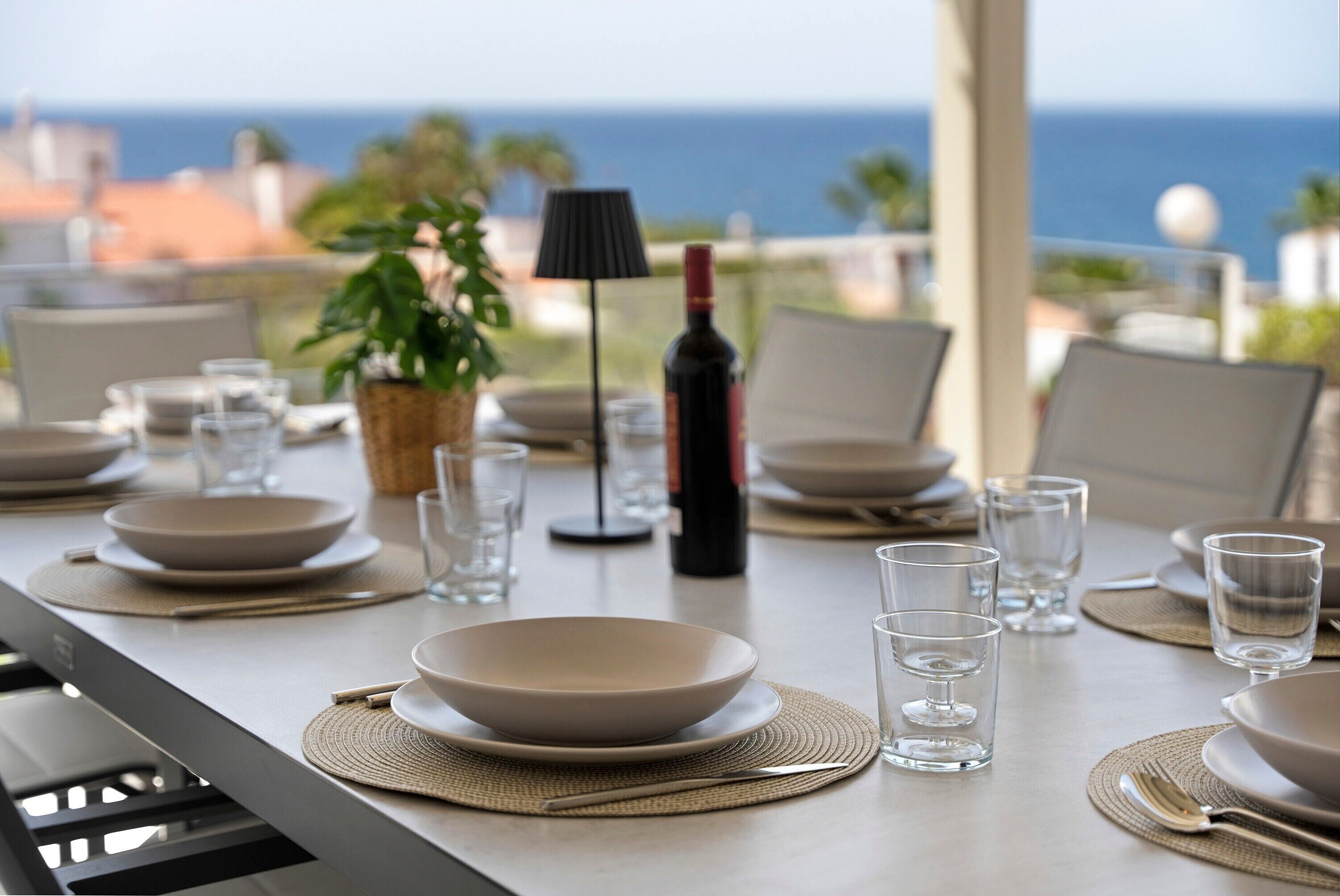 Una tavola apparecchiata per la cena con vista sull'oceano, una bottiglia di vino e una lampada.