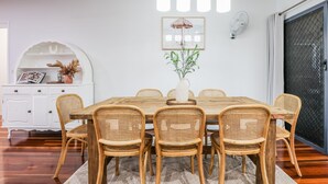 Ein Essbereich mit einem Holztisch und sechs Korbstühlen, einem weißen Schrank mit Dekorationsobjekten und einem gerahmten Bild an der Wand.