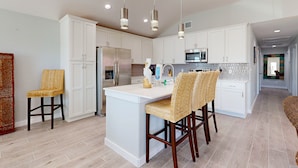 A modern kitchen with white cabinetry, a central island, and a seating area with wicker chairs. - Private Pool, Pet Friendly, Parking for 5 Vehicles (Port Aransas)