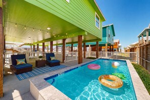 Un área de piscina con sillones de descanso, una terraza cubierta y una piscina azul cristalina.