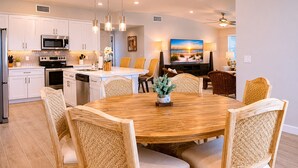 A modern kitchen with white cabinets, stainless steel appliances, and a dining area with a wooden table and wicker chairs. - Private Pool, Pet Friendly, Parking for 5 Vehicles (Port Aransas)