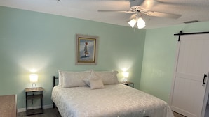 Une chambre à coucher avec un lit, deux lampes de chevet, un ventilateur de plafond, un tableau et une armoire.