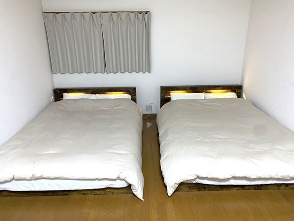 Dos camas individuales con cabeceros de madera, una cortina gris y una pared blanca.