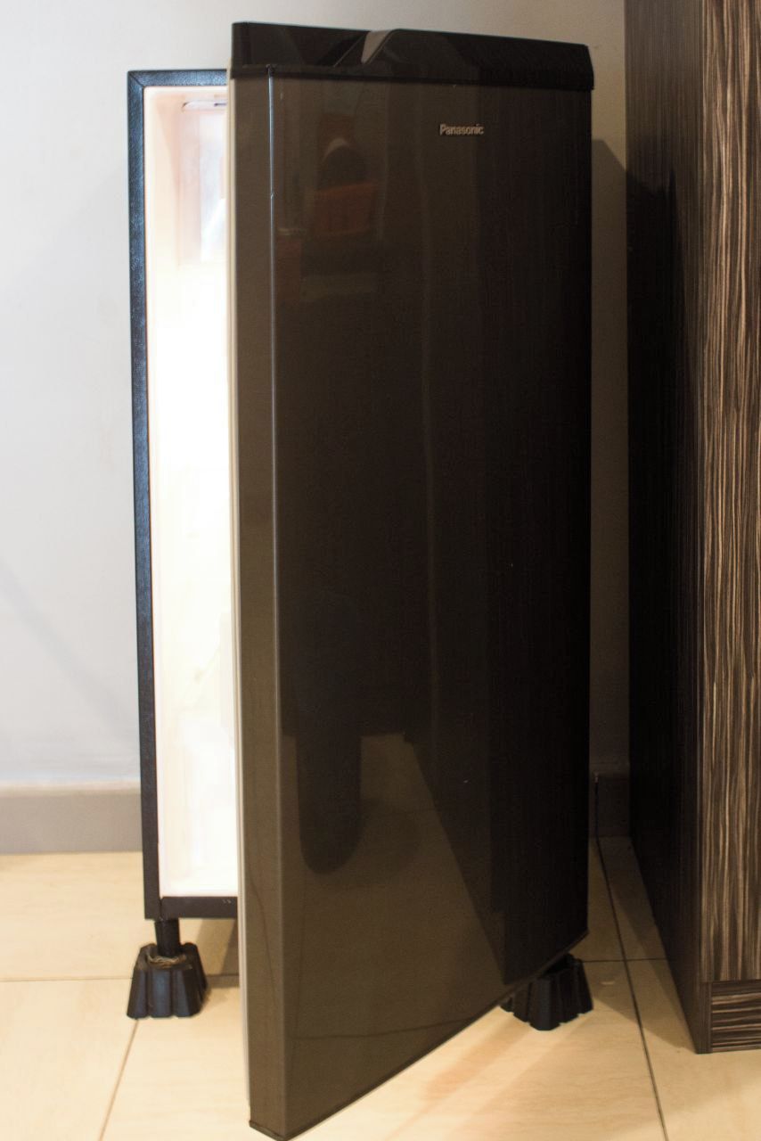 A black refrigerator with the brand name 'Panasonic' on it, placed on a tiled floor next to a wooden cabinet.