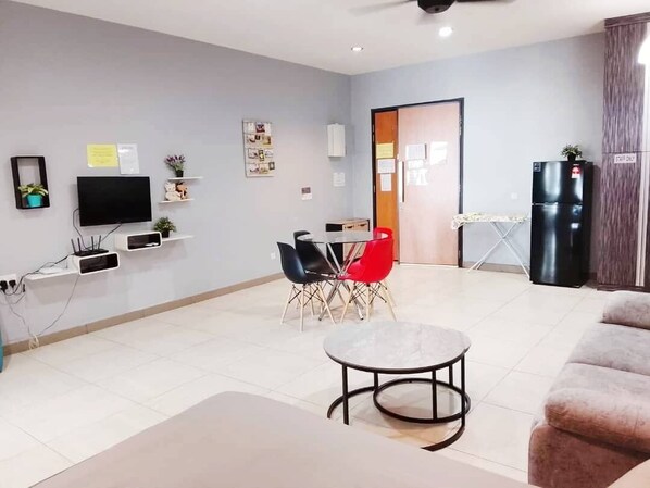 A modern living room with a flat-screen TV, a dining table with chairs, a sofa, and a refrigerator.