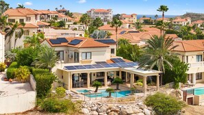 Un barrio residencial con casas que tienen techos de tejas rojas, paneles solares y una piscina.