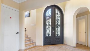 Una imponente entrada con puertas dobles, una escalera que conduce a un piso superior y un suelo de baldosas.