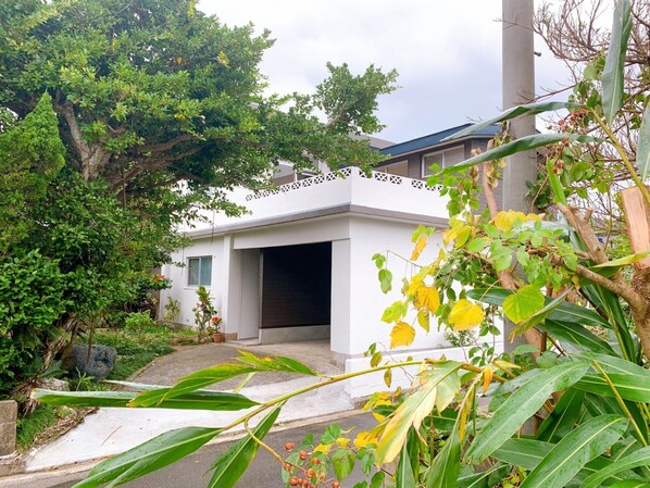 Une maison moderne à l’extérieur blanc, dotée d’un garage et entourée d’une végétation luxuriante.