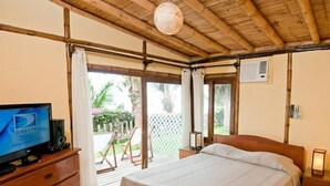 A bedroom with a wooden ceiling, a bed, a TV on a wooden dresser, and a view of a garden through a sliding door.