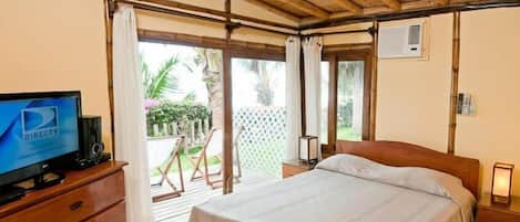 A bedroom with a wooden ceiling, a bed, a TV on a wooden dresser, and a view of a garden through a sliding door.