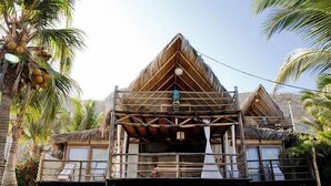 A traditional wooden structure with a thatched roof, surrounded by palm trees and a stone wall.
