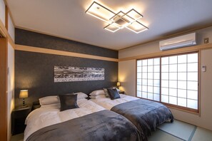 Two beds with dark bedding, a large window, and a ceiling light fixture.