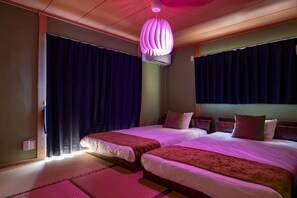Ein Hotelzimmer mit zwei Betten, einem Deckenventilator und einem großen Fenster mit Vorhängen.